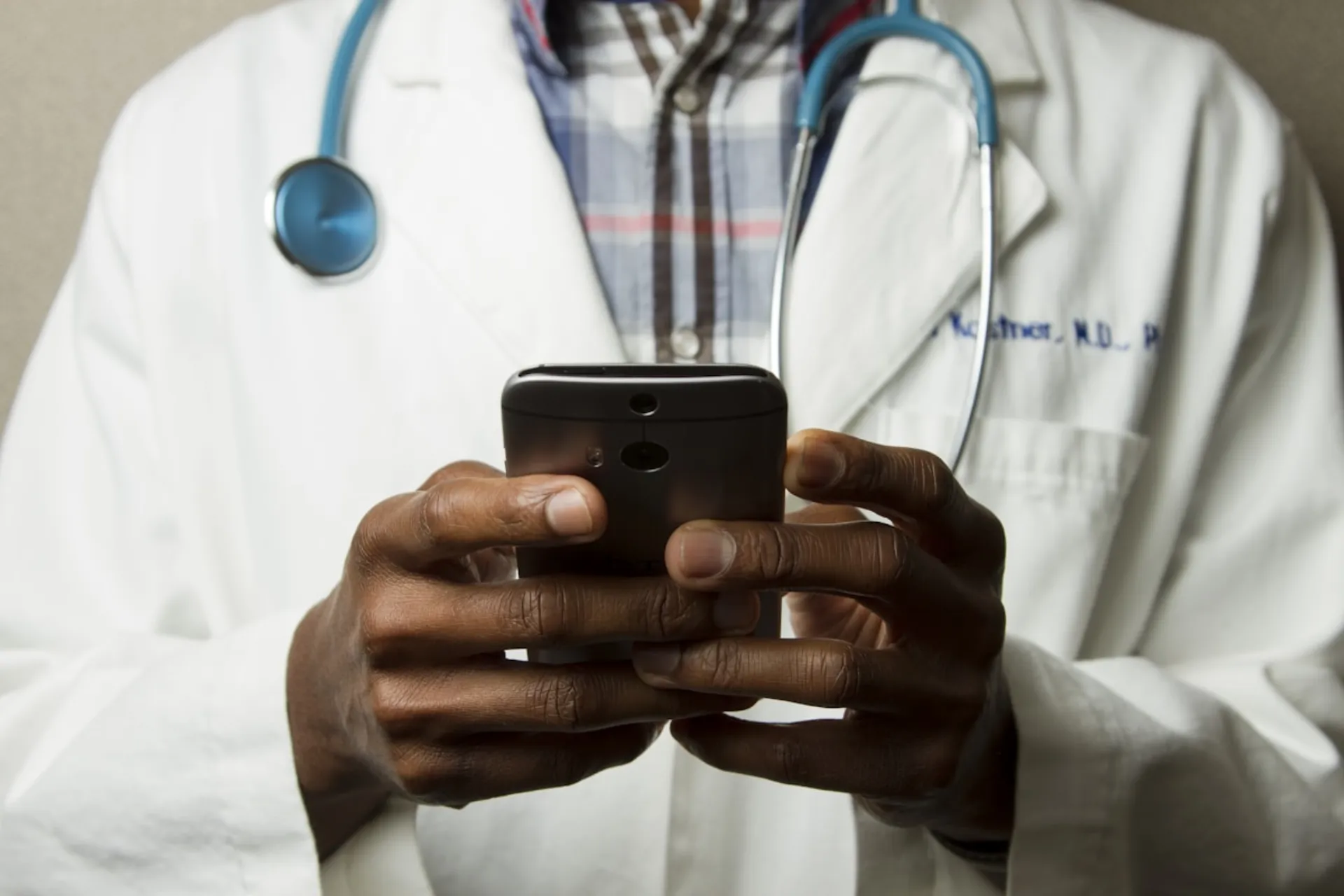 A physician in a white coat reading a message on a phone between appointments