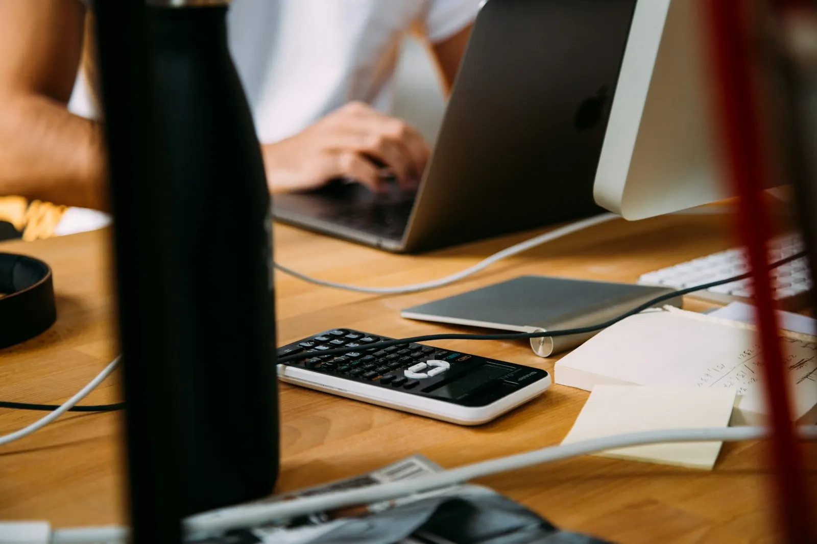 Hands working at a laptop on a desk beside a calculator and a phone